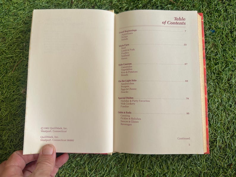 May include: Open cookbook with a red patterned cover, displaying the table of contents. Sections include appetizers, main fare, side courses, and special dishes. The book is open to pages with text and a copyright notice.