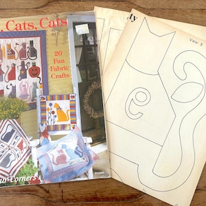 Op de afbeelding: Een stapel vintage knutselboeken en patronen met kattenontwerpen. De boeken hebben titels als "Cats, Cats, Cats" en "20 Fun Fabric Crafts". De patronen bevatten lijntekeningen van katvormen.