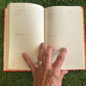May include: Open cookbook with lined pages, featuring prompts for recipes, ingredients, and oven directions. The book has a red cover with a floral design. The book is open to pages 66 and 67.