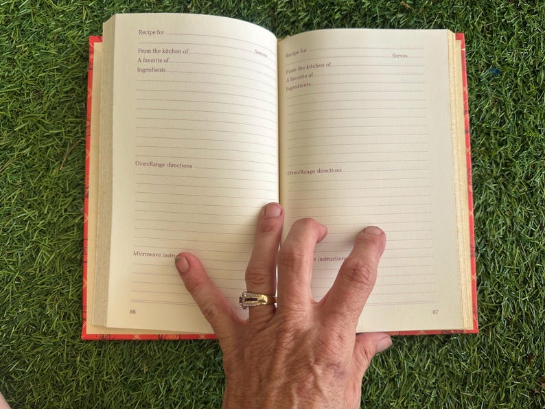 May include: Open cookbook with lined pages, featuring prompts for recipes, ingredients, and oven directions. The book has a red cover with a floral design. The book is open to pages 66 and 67.
