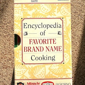 May include: A yellow and white book titled "Encyclopedia of Favorite Brand Name Cooking" with various brand logos including Hershey's, A1 Steak Sauce, Filippo Berio, Dole, Miracle Whip, Kingsford, and DiGiorno.