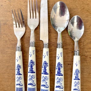 May include: Set of five silver-tone flatware with white handles featuring a blue and white floral design. The set includes a knife, two forks, and two spoons.