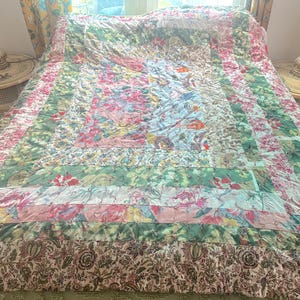 Peut inclure: Une courtepointe florale colorée avec un motif patchwork. La courtepointe présente une variété de motifs et de couleurs, notamment du rose, du vert et du blanc. La courtepointe est sur un lit et semble être faite à la main.