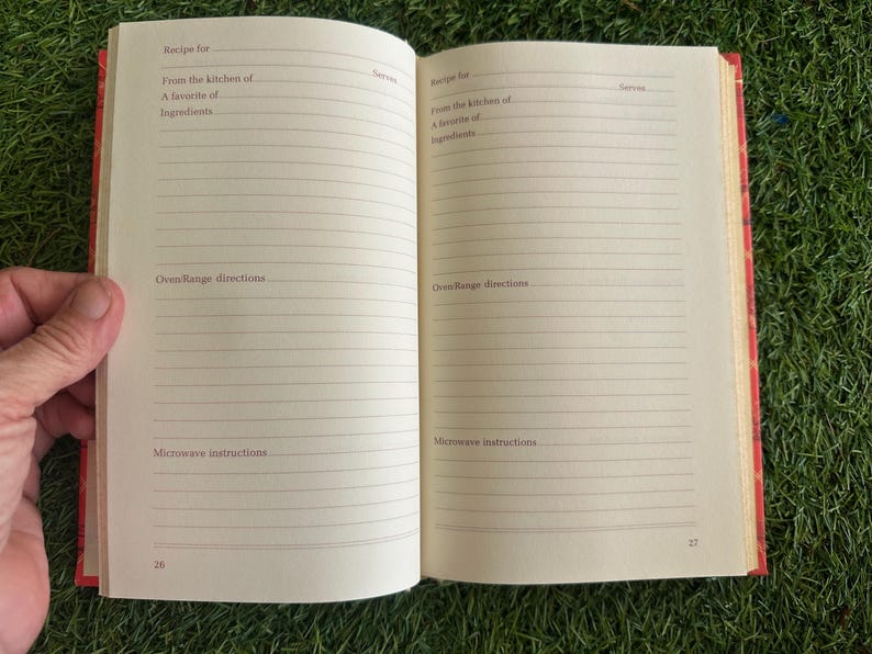 May include: Open recipe book with lined pages. The book is open to a spread with prompts for recipe details: recipe name, kitchen source, favorite ingredients, oven/range directions, and microwave instructions. The book's cover is red.