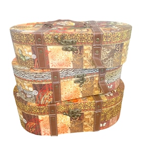 May include: A stack of three oval-shaped storage boxes featuring a multi-patterned design with leopard print, floral motifs, and script text. Each box has brown faux leather straps, brass-colored metal latches, and a matching handle on the top box.