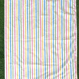 May include: A white sheet featuring vertical stripes in a variety of colours: blue, green, yellow, and pink. The stripes are evenly spaced and run the length of the sheet. The sheet is laid out on a green surface.