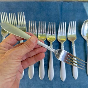 May include: A set of eight silver-plated forks and a spoon. The forks and spoon have ornate handles and are arranged on a blue surface.