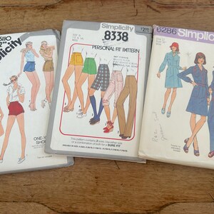May include: Three vintage Simplicity sewing pattern envelopes. The patterns feature illustrations of women's clothing designs, including shorts, skirts, and jumpsuits. The envelopes are white with colorful illustrations and text, and the patterns are from the 1970s.