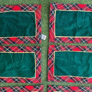 Könnte beinhalten: Sechs rechteckige Tischsets. Jedes hat eine dunkelgrüne Mitte, die von einem goldenen Rand und einem rot-schwarz-weiß karierten Muster umrahmt ist. Die Tischsets sind auf einer grünen Oberfläche angeordnet.