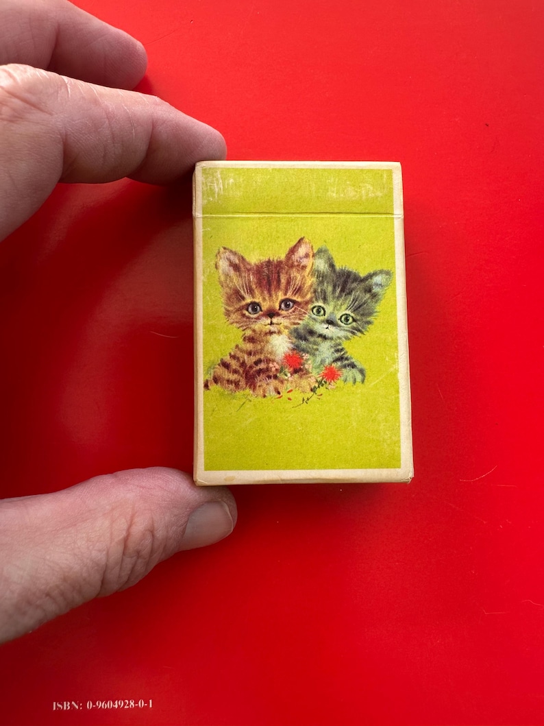 May include: A vintage matchbox with a lime green background featuring two kittens. One kitten is brown and the other is gray. The matchbox has the ISBN 0-9604928-0-1 printed on the bottom.
