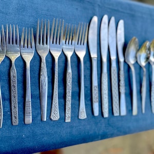 May include: A set of silver cutlery, including forks, knives, and spoons, laid out on a blue fabric surface.
