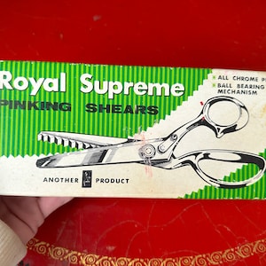 Pode incluir: Uma caixa vintage de tesouras de picote Royal Supreme com fundo listrado verde e branco. As tesouras são cromadas com um mecanismo de rolamento de esferas. A caixa diz "Another  Product".