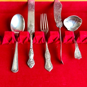 May include: A set of five silver-plated utensils, including a spoon, fork, butter knife, and two serving spoons, are displayed in a red velvet-lined case.