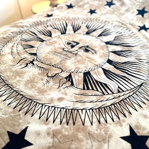 May include: A tapestry featuring a black and white illustration of a sun and moon with a star pattern background. The sun and moon are stylized with faces and the sun has rays emanating from it.