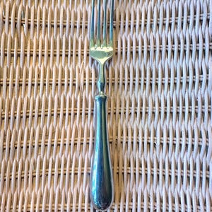 May include: A polished silver-toned metal fork featuring four slender tines and a smooth, rounded handle that tapers toward the neck. The utensil has a reflective, metallic finish and a simple, clean design with no decorative patterns or engravings.