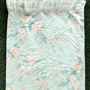 Peut inclure: Un drap de lit floral vert clair avec un bord supérieur à volants. Le drap présente un motif répété de fleurs jaunes et blanches avec des feuilles vertes. Le bord à volants a une bordure en dentelle blanche.