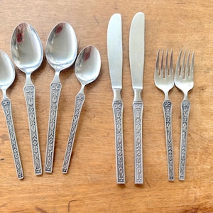May include: A collection of vintage silverware, including spoons, knives, and forks, arranged on a wooden surface. The silverware has ornate, detailed handles and a polished, reflective finish. The set includes various spoon sizes, knives, and forks.