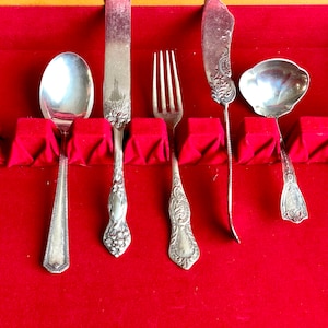 May include: A set of five silver-plated utensils, including a spoon, fork, butter knife, and two serving spoons, are displayed in a red velvet-lined case.