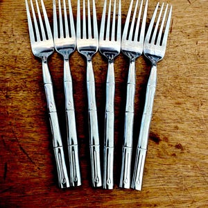 May include: A set of six stainless steel forks arranged in a row. Each fork features a polished finish and a handle designed with a textured, segmented pattern that mimics the appearance of bamboo stalks, ending in a rounded tip.