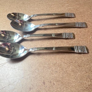 May include: Four silver spoons with ornate designs on the handles. The spoons are arranged in a row, with the handles pointing to the right.