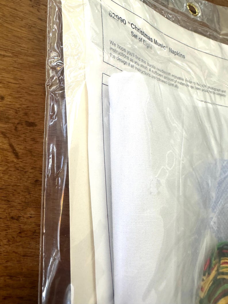 Może przedstawiać: Białe opakowanie z białą serwetką w środku. Na opakowaniu widnieje napis "82990 "Christmas Music" Napkins Set of Eight".