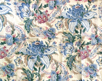 May include: Close-up of a fabric with a floral pattern. The design features large blue flowers with white accents, interspersed with smaller pink and blue blossoms and paisley shapes, all set against a cream background.