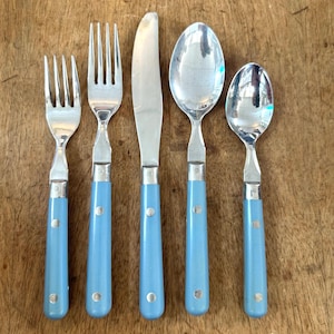 May include: A five-piece cutlery set comprising two forks, a knife, and two spoons. The light blue handles have silver detailing. The set is arranged on a wooden surface.