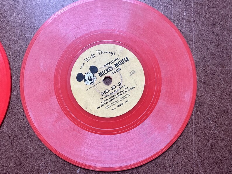 May include: Red vinyl record with a label featuring Mickey Mouse and the text "From Walt Disney's Official Mickey Mouse Club" and "Sho-Jo-Ji (A Japanese Play Song)".