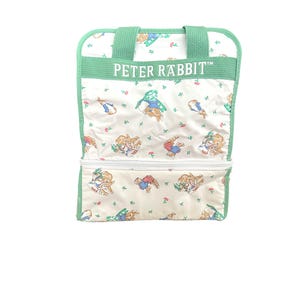 May include: A white rectangular bag with a green trim and handles, featuring a repeating pattern of Peter Rabbit characters and small flowers. The text PETER RABBIT is printed in white on a green horizontal band across the upper section of the bag.