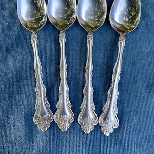 Può includere: Quattro cucchiai d'argento con manici decorati. I cucchiai hanno una finitura lucida e sono disposti in fila su uno sfondo blu.