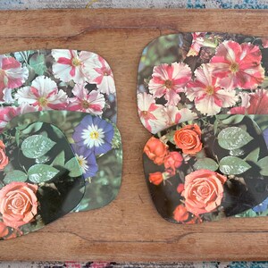 May include: Set of floral coasters featuring vibrant blooms. The coasters showcase a variety of flowers, including roses, petunias, and morning glories, in shades of pink, red, white, and purple. The coasters are arranged on a wooden surface.