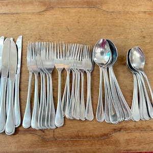 May include: A collection of stainless steel silverware, including knives, forks, and spoons, arranged on a wooden surface. The silverware has a simple, elegant design, with smooth handles and a polished finish. The set includes approximately 10 knives, 20 forks, and 10 spoons.