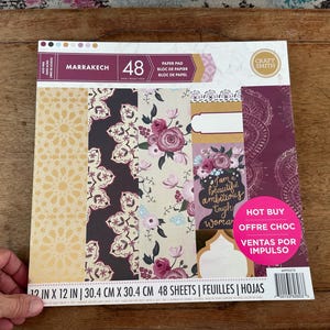 May include: A 12 inch by 12 inch Craft Smith Marrakech paper pad containing 48 sheets. The cover features various patterns including gold geometric designs, dark floral motifs, and a card with the text I am a beautiful ambitious tough woman.