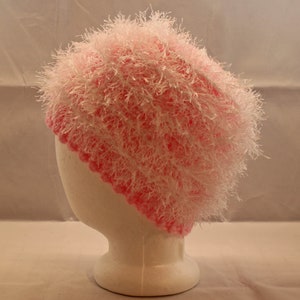 Puede incluir: Un gorro de punto rosa y blanco con textura peluda. El gorro se muestra en una cabeza de maniquí blanca.