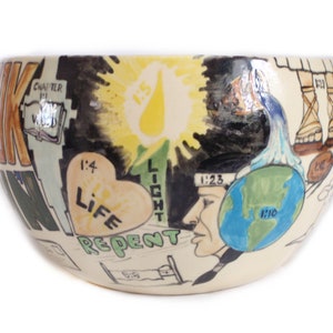 May include: A ceramic bowl with a colourful, hand-painted design. The bowl features a heart with the words "1:4 Life Repent", a sun with the number "1:5", a globe with the numbers "1:23" and "1:10", and the word "LIGHT".