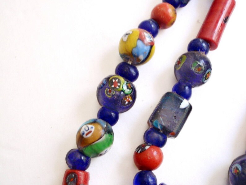 May include: Close-up of a colorful beaded necklace. The necklace features a variety of beads, including round, cylindrical, and rectangular shapes. The beads are in shades of blue, red, yellow, and green, with intricate patterns and designs.