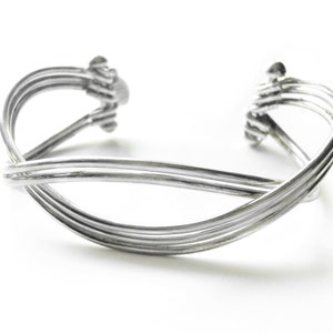 May include: A silver bangle bracelet with a woven design. The bracelet is made of four strands of metal that are twisted together.