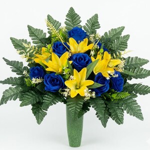 May include: A vibrant floral arrangement featuring blue roses and yellow lilies, accented by green fern leaves. The bouquet is presented in a green vase, creating a striking contrast against the white background. A beautiful display of artificial flowers.