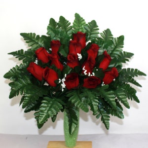 May include: A bouquet of red roses with green fern leaves in a green vase. The vase is on a wooden base.