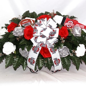 May include: A floral arrangement featuring red, white, and silver roses, green foliage, and a large bow with the Ohio State Buckeyes logo. Includes a football and pennant with the team name.