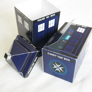 May include: A blue and white cardboard box shaped like the TARDIS from Doctor Who. The box has the words "Police Box" on the side and "Candy Box" on the front. The front of the box also has a blue and white starburst design.
