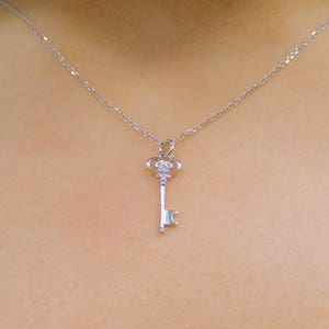 May include: A silver key necklace with a small, clear crystal on the top of the key.