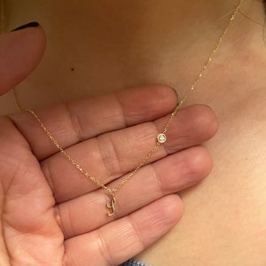 Può includere: Una collana con catena d'oro con un piccolo accento di diamante e un ciondolo con la lettera 'J' in corsivo.