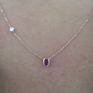 May include: A delicate gold chain necklace with a small red gemstone and a smaller clear gemstone.