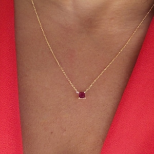 May include: A delicate gold chain necklace with a small, square-shaped ruby pendant.