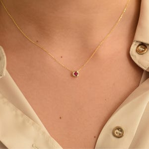 May include: A delicate gold chain necklace with a small, round ruby pendant.