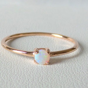 May include: A delicate rose gold ring with a small, round opal gemstone.