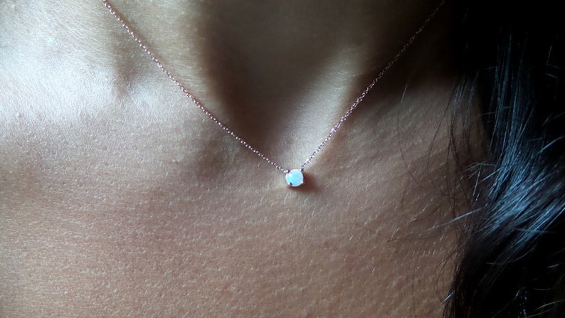 Puede incluir: Un delicado collar de cadena de plata con un peque&ntilde;o colgante redondo de &oacute;palo blanco.
