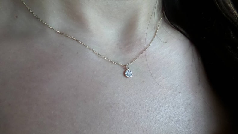 Op de afbeelding: Een delicate gouden ketting met een klein, rond hangertje bezet met kleine diamanten.
