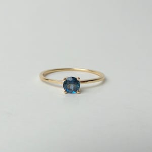 May include: A gold ring featuring a blue gemstone. The ring is simple and elegant.